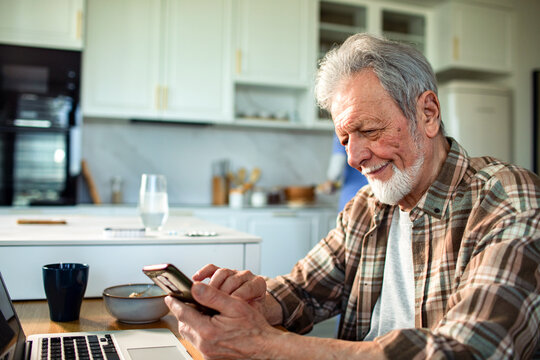 Smiling senior man using smartphone at kitchen table