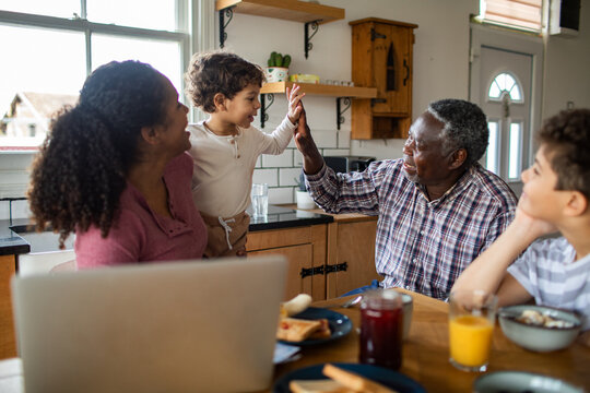 Grandfather high fives child at family breakfast in kitchen