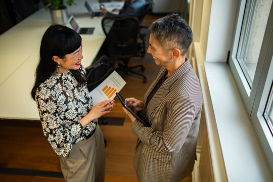 Two businesswomen discussing sales report by office window