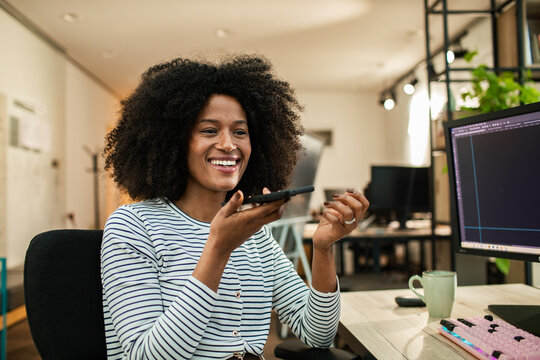 Smiling woman using voice assistant at office desk