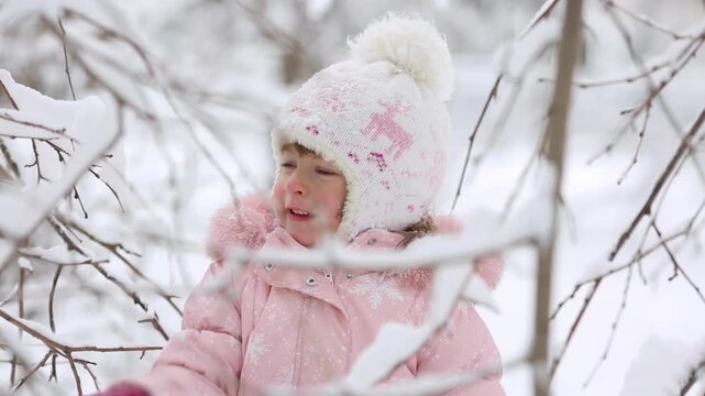 A child is having fun outdoors in winter forest. A little girl plays in a nature park against a snow covered trees background. Slow motion