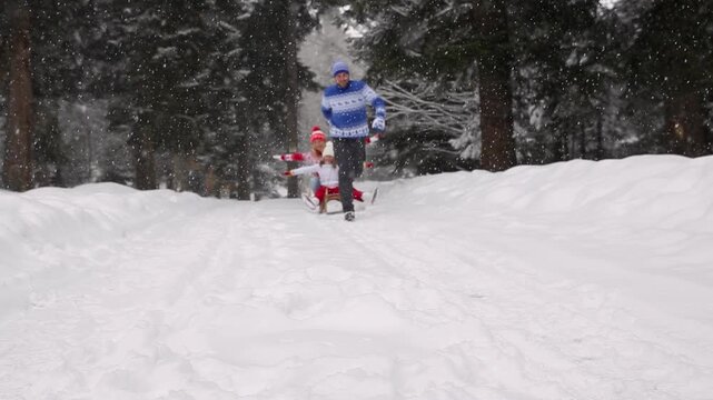 People are having fun outdoors in winter forest. A family rides a sleigh in a nature park against a snow covered trees background. Healthy lifestyle and Christmas holidays concept.