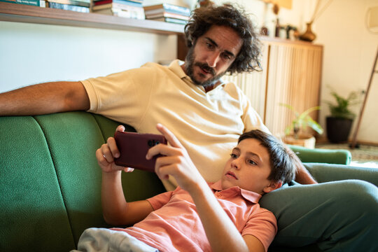 Father and son using smartphone on couch in living room