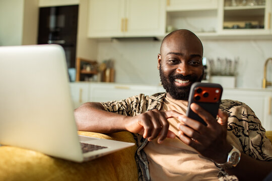 Smiling man using smartphone on sofa at home