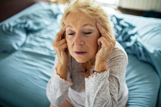 Senior woman touching temples with headache in bedroom