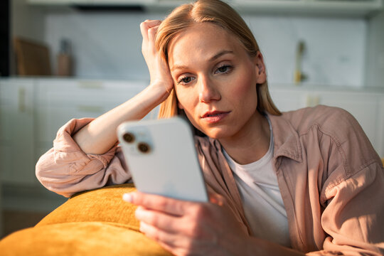 Young woman reading smartphone with worried expression at home