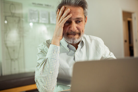 Middle-aged man stressed at laptop in home office