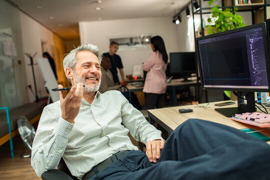 Smiling senior designer on speakerphone in modern office