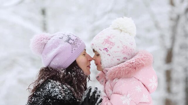 Mother and child are having fun outdoors in winter forest. A family plays in a nature park against a snow covered trees background. Slow motion