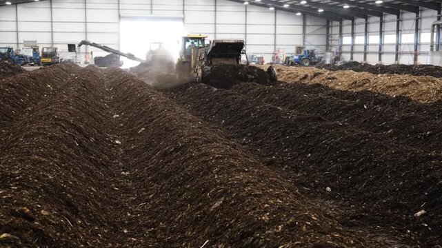 Tractor turning large windrows of organic waste inside an industrial composting facility