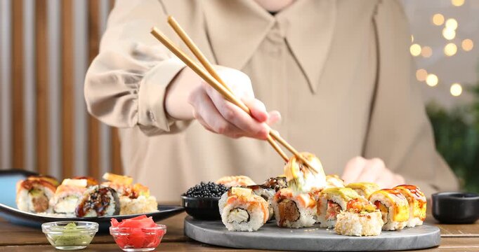Woman taking tasty sushi roll with chopsticks at wooden table, closeup
