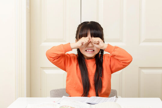 Frustrated little girl rubbing her eyes while crying over difficult school homework.
