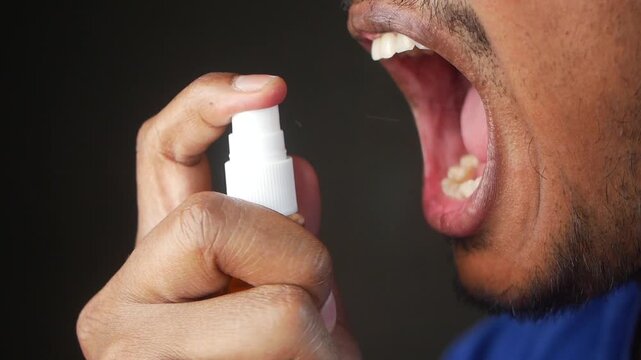 A man using a throat spray to alleviate a sore throat, showing close-up of his mouth and the spray in action