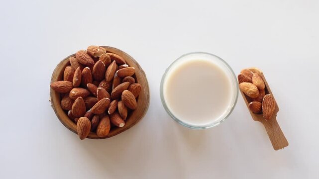 Top view of almond milk glass and nuts in wooden bowl on white background with smooth camera motion