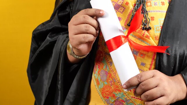 Graduation ceremony student holding diploma scroll with red ribbon in black academic robe