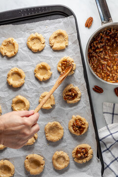 A hand placing some pecan pie mixture into the centre of a pie cookie shell.