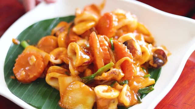 Close up footage of stir fried squid and carrots in a savory orange sauce served on a banana leaf.