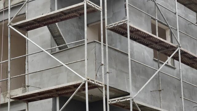 Low angle shot of construction site featuring building facade with extensive metal scaffolding and grey concrete walls during renovation