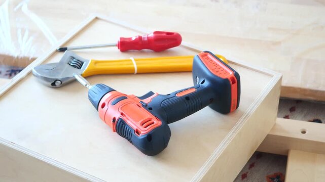 Close-up shot of a cordless drill, screwdriver, and wrench laying on wooden boards, depicting DIY home improvement and renovation tools