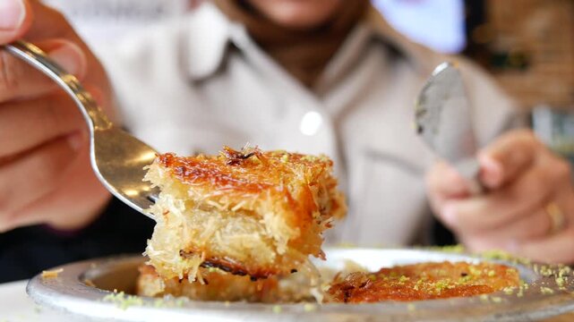 A close-up shot of hand holding a fork with delicious traditional turkish dessert kunefe on it and knife in other hand