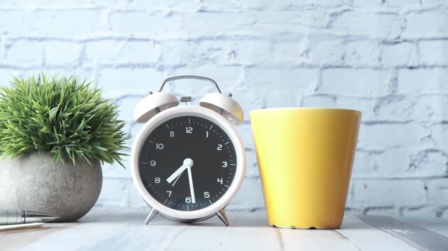 Close up alarm clock ticking showing passing time next to yellow cup and plant
