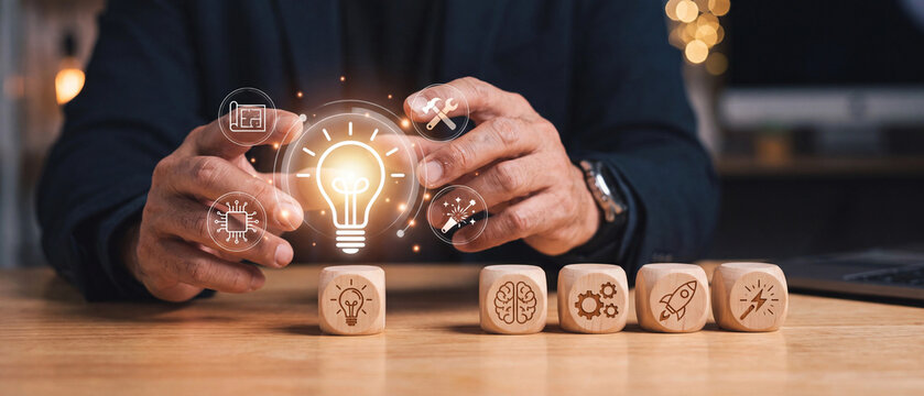 Businessman holding a glowing light bulb icon with business strategy icons on wooden blocks, concept of innovation and creativity