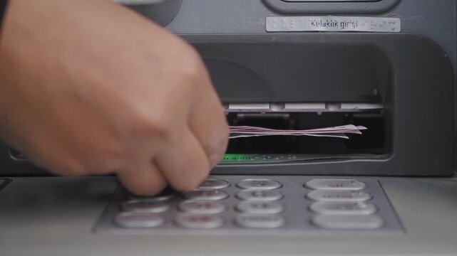 Hand inserting stack of Turkish lira banknotes into ATM money slot