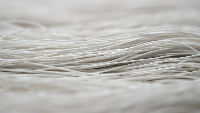 Close up of many thin white threads or strings arranged in parallel lines, creating a textured abstract background with soft focus