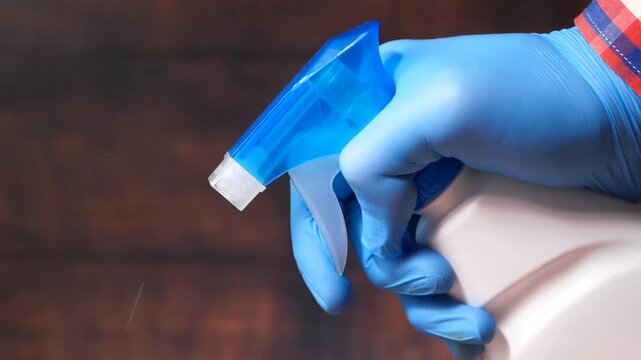 Close up of hand wearing blue glove spraying disinfectant from bottle for cleaning
