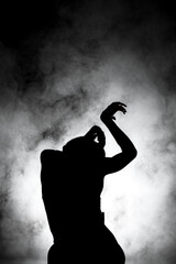 Obraz premium silhouette modern ballet dancer posing on dark background with smoke