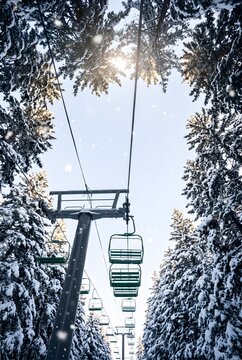 Vertical photograph looking steeply upward from directly beneath a chairlift line at an alpine ski area, a row of empty chairs receding upward into the frame growing smaller with perspective.