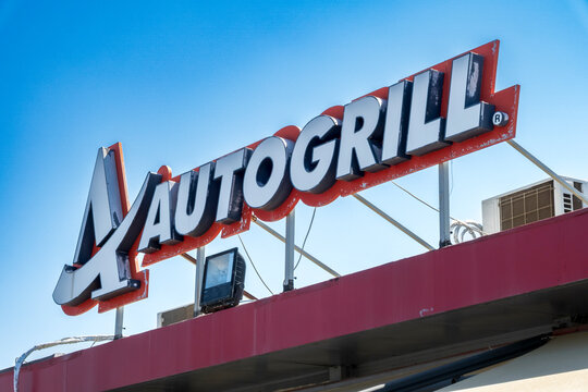 Milazzo - ME - IT - Sep 09, 2026: Autogrill rooftop sign with large white and black lettering on a red backing above a red building facade, photographed from below against a blue sky overhead.