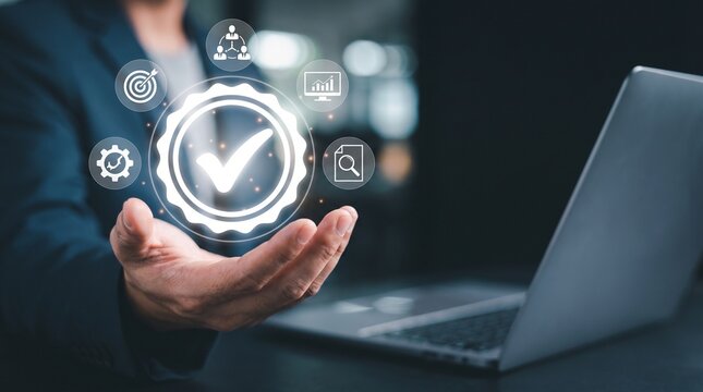 Professional businessman holding a glowing checkmark icon symbolizing quality management standards and digital compliance processes while using a modern silver laptop in a dark office