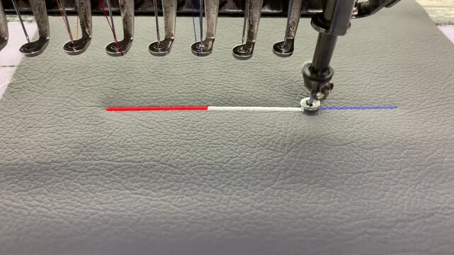 Industrial embroidery machine stitching above on textured synthetic leather material.