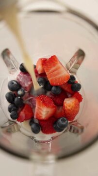 Hands Pouring White Milk into Large Glass Filled with Assorted Fresh Fruit Pieces