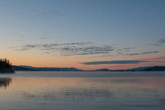 Orange sunrise and mist over lake with mountains in background