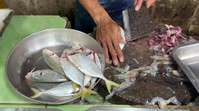 Cutting and cleaning fresh raw fish on a wooden chopping block in a traditional market