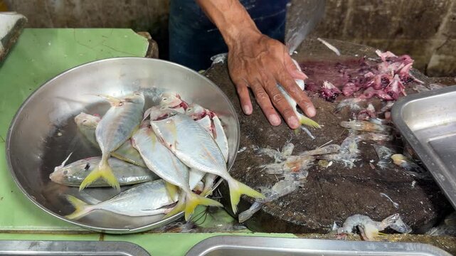 Vendor cleaning yellowtail scad fish on a cutting block in traditional market