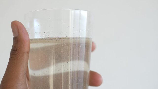 Holding glass of dirty contaminated water with visible sediments against white background