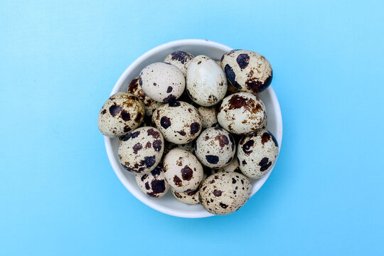 Top view A collection of speckled quail eggs in a brown bowl isolated on a blue background.