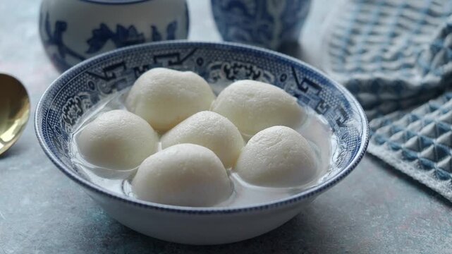 Rasgullas served in a bowl with water and a blue patterned napkin