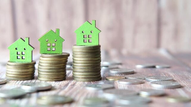 House models on coin stacks displaying a rising graph with coins spread around on a wooden table, symbolizing increasing property values and investment growth in real estate market, dynamic footage
