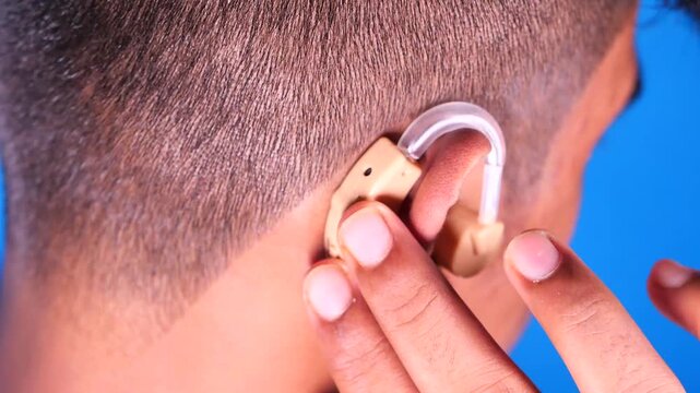 Close up of a person inserting a hearing aid into their ear, improving sound amplification
