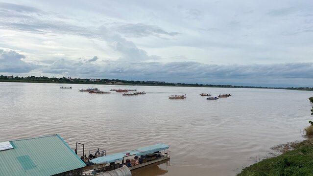 Boats on the Mighty River: A serene expanse of a wide, muddy river under a cloudy sky, dotted with several boats and a small dock, depicting a peaceful riverside scene.