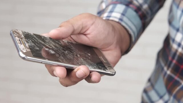 Close up of man holding broken smartphone with cracked screen in hand