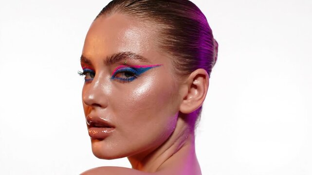 Young woman showcasing vibrant neon graphic eyeliner makeup look with dewy skin texture against bright white background