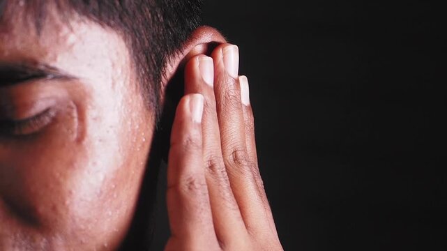 Young man experiencing ear pain and discomfort against black background