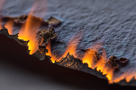 Burning Paper Edge: Extreme close-up of a piece of paper's edge catching fire, showcasing the intricate texture of the burning material and the vibrant orange flames licking its surface.