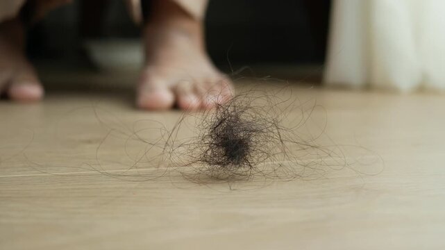 Hair loss problem shown by pile of fallen hair on floor with person standing in background