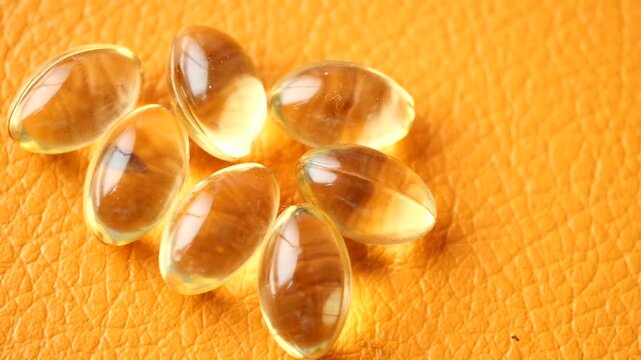Close up of yellow omega 3 fish oil capsules rotating on an orange background, dietary supplements and health concept